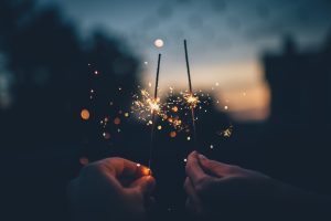 Hands holding two lit sparklers in twilight